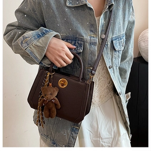 Détail d'un sac en cuir marron foncé avec boucle dorée et breloque petit ours