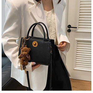 Détail du sac en cuir noir texturé avec fermoir doré et breloque ours en peluche marron