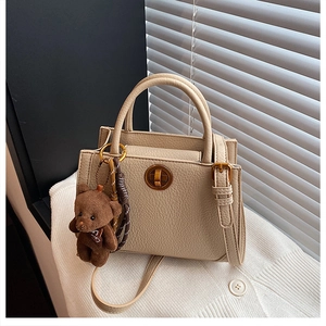 Détail d'un sac à main beige avec fermoir doré en métal et pendentif ours en peluche marron