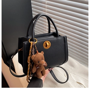 Détail du sac à main en cuir noir texturé avec fermoir doré et breloque ours en peluche