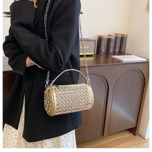 Detail of a sparkling gold cylinder bag with rhinestones shown on a black suit