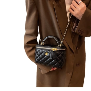 Quilted black mini crossbody bag with gold floral accent and chain strap worn on blazer