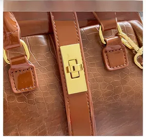 Detail of the golden rectangular buckle and hardware on the brown crocodile texture handbag