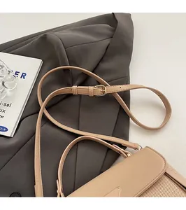 Detail of beige shoulder bag with woven texture, metal logo, and adjustable strap
