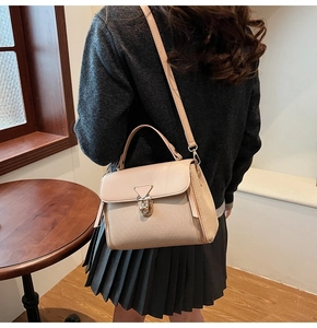 Chic beige crossbody bag with gold triangle clasp shown on a model in a cozy interior