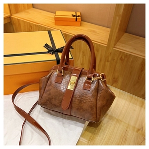 Detail of brown crocodile pattern handbag with golden twist lock and round handles