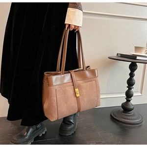 Detail of a large brown suede tote bag featuring contrast leather trim and a gold twist lock