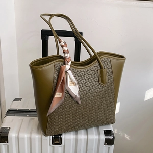 Grande borsa tote verde oliva con trama intrecciata e sciarpa floreale su una valigia