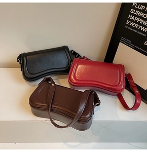 Three wavy leather shoulder bags in black, burgundy and dark brown on a stone surface