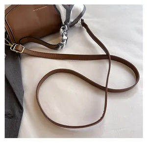 Detail of a brown leather crossbody bag featuring an adjustable strap and decorative scarf