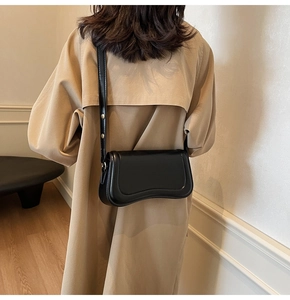 Detail of black leather crossbody bag with wave-shaped bottom on a beige coat