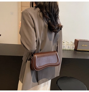 Detail of dark brown leather crossbody bag with unique wavy base and adjustable strap