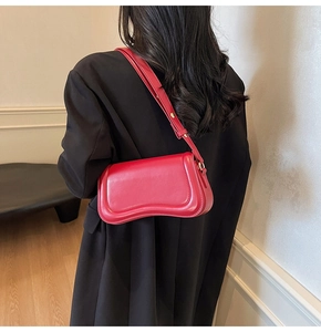 Detail of red glossy leather bag with curved bottom and gold buckle on black blazer