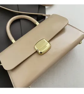 Détail d'un sac à main beige minimaliste avec fermoir doré et poignée arrondie