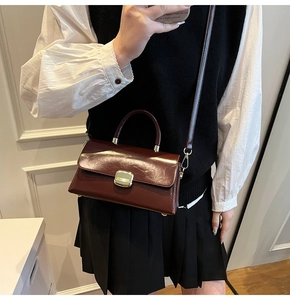 Détail d'un sac à main bordeaux structuré avec fermoir doré sur un mannequin femme