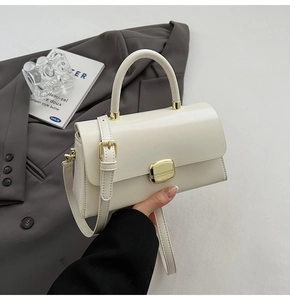 Détail du sac à main blanc crème avec fermoir doré posé sur un blazer gris