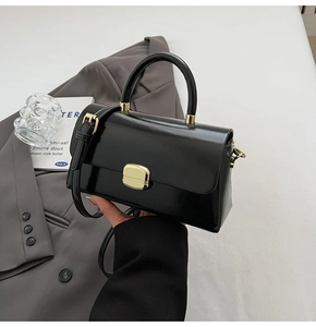Détail d'un sac à main noir brillant avec fermoir doré et poignée élégante