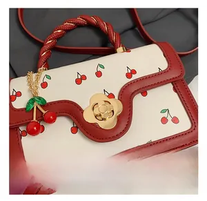 Close-up of golden floral clasp and cherry pendant on white leather handbag