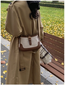 Outdoor shot of a vintage canvas and leather crossbody bag styled with a trench coat