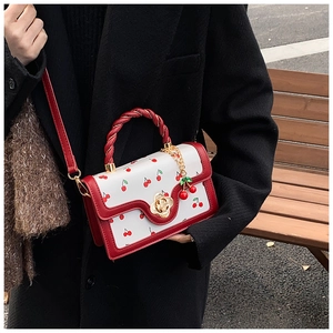 Detail of a cherry print handbag with a red twisted handle and gold flower clasp
