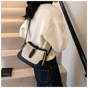 Detail of canvas crossbody bag with black leather trim and gold buckle worn by model