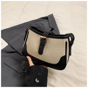 Detail of canvas crossbody bag featuring black leather trim and gold metal buckle