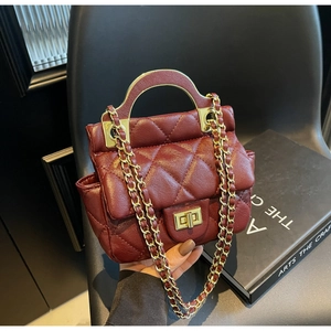Detail of burgundy quilted crossbody bag with gold handle and chain strap on black background