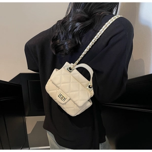 Rear view of a model wearing a beige quilted small crossbody bag with gold chain strap