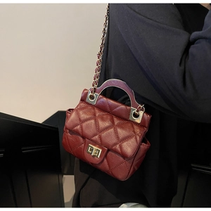 Detail of red quilted crossbody bag with gold chain strap and metal arched handle