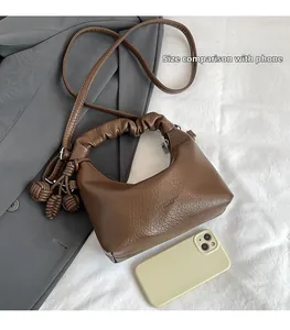 Detail of coffee brown leather handbag with ruched handle and size comparison with phone