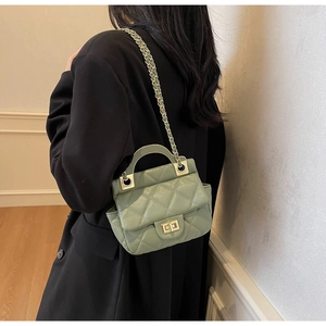 Detail of sage green quilted chain bag worn over a black blazer in a minimalist setting