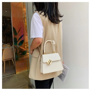 Chic beige trapezoid handbag featuring a large gold metal buckle and knotted handle detail
