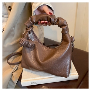 Detail of brown lychee grain leather handbag with woven charms and ruched handle