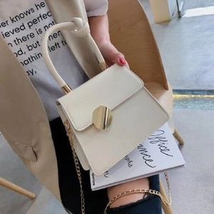 Detail of cream square handbag with gold twist handle and metallic circular lock closure