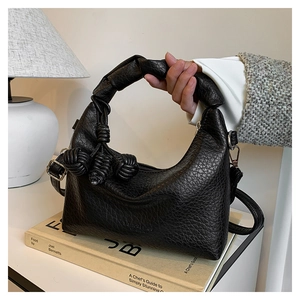 Detail of black pebbled leather handbag with knotted rope handle and woven charms on books