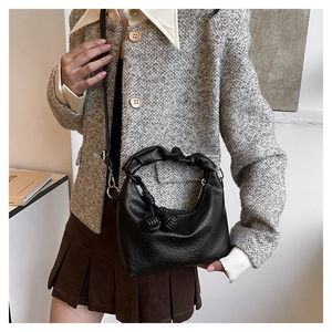 Detail of black lychee grain leather handbag with ruched handle and knot decorative accents