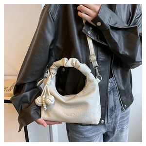 Detailed shot of beige half-moon pleated handbag with braided pom-pom charms and leather texture