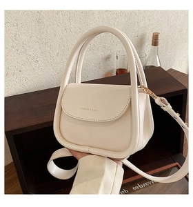 Detail of cream faux leather handbag with circular handle and gold-tone metal hardware