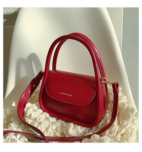 Detail of red leather crossbody bag with gold text on white fabric and chair background