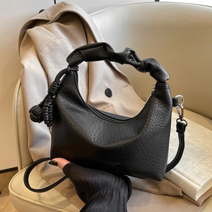 Minimalist black crescent shoulder bag with pleated handle and woven charm on a beige seat