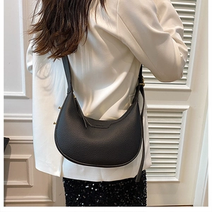 Close-up of black lychee-textured leather crescent bag with golden metal buckle details