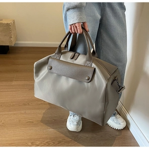 Detailed view of the large greige travel bag with brown leather handles and side buckles