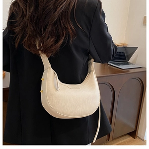 Chic cream lychee grain leather crescent bag with gold rivets worn by a model