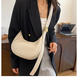 Close-up of off-white lychee leather handbag with golden buckle and wide strap on model
