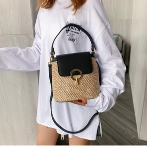 Détail du sac seau en paille avec garniture en cuir noir et grande boucle en métal doré