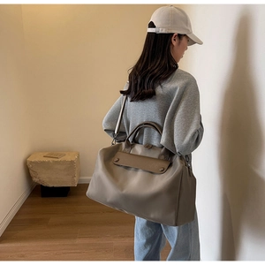 Side view of large khaki travel tote bag on model showing shoulder strap and leather handle