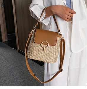 Détail d'un sac seau en paille avec rabat en cuir marron et fermoir doré sur modèle