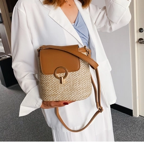Détail du sac seau en paille avec rabat en cuir marron et fermoir rond doré