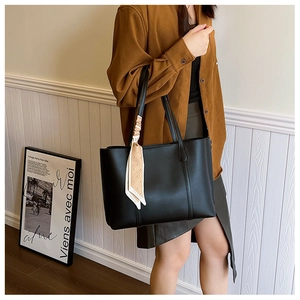 Detail of a black leather tote bag with a beige polka dot scarf handle shown on shoulder