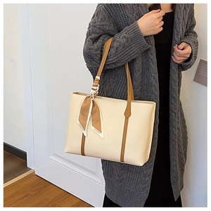 Detail view of a beige leather tote bag with brown straps and a decorative floral silk scarf